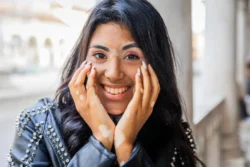 Portrait of a smiling teenage girl with vitiligo touching her face with her hands. / What Causes Vitiligo? Signs, Types, Causes & Diagnosis / What Is Vitiligo? / Common signs and symptoms / Types of vitiligo / What Causes Vitiligo? / Is Vitiligo Hereditary? / Common Myths and Misconceptions / Can Emotional Stress Cause Vitiligo / Associated Medical Conditions / Diagnosing Vitiligo