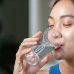 Active woman enjoying a refreshing drink, promoting hydration and wellness in a modern setting. - Does Drinking Water Help With Acne? - Palm Beach Dermatology Gruop