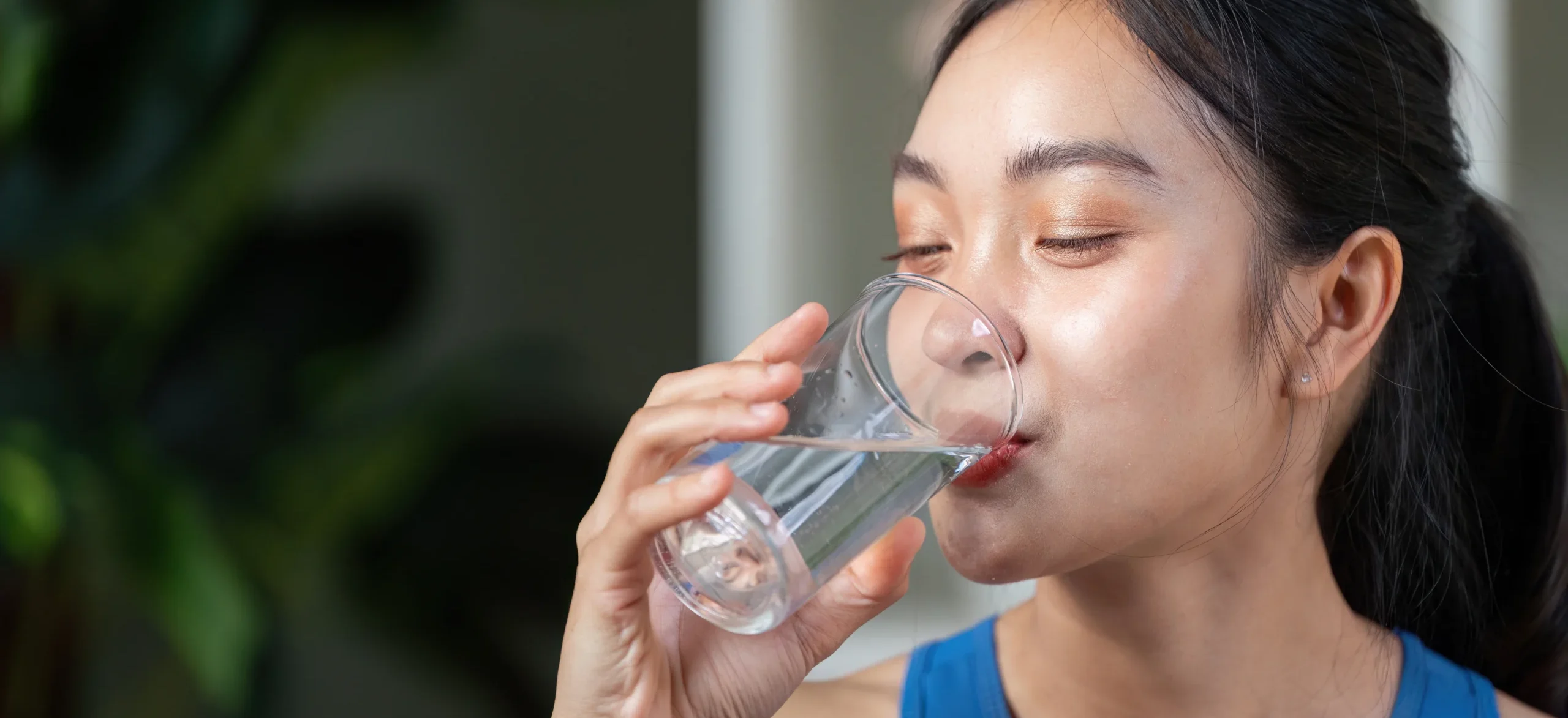 Active woman enjoying a refreshing drink, promoting hydration and wellness in a modern setting. - Does Drinking Water Help With Acne? - Palm Beach Dermatology Gruop
