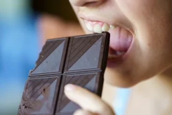 young girl with mouth open about to eat chocolate - Does Chocolate Cause Acne? A Complete Guide