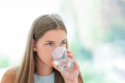 Active woman enjoying a refreshing drink, promoting hydration and wellness in a modern setting. - Does Drinking Water Help With Acne? - Palm Beach Dermatology Gruop