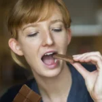 young woman eating chocolate - Does Chocolate Cause Acne? A Complete Guide - Palm Beach Dermatology Group