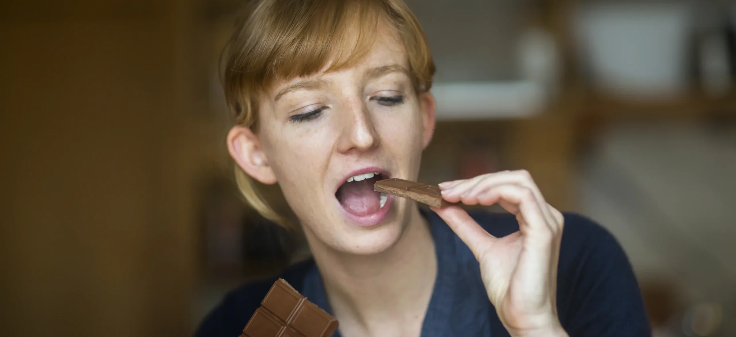 young woman eating chocolate - Does Chocolate Cause Acne? A Complete Guide - Palm Beach Dermatology Group