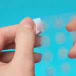 close up round acne patch on finger on blue - Do Pimple Patches Work on Blackheads?